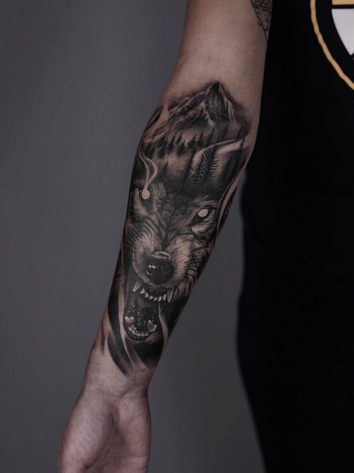 Majestic wolf tattoo surrounded by trees and mountains, evoking a sense of strength and natural beauty.
